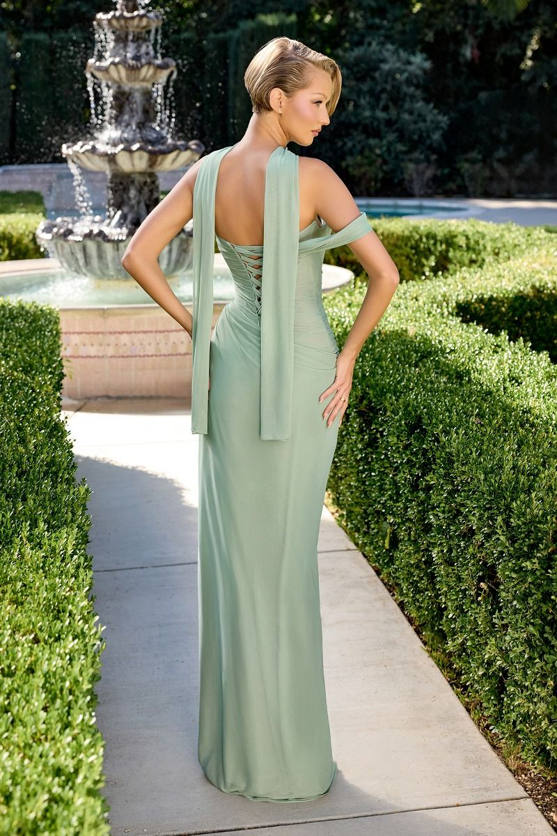 Woman in a light green evening gown standing in a garden with a fountain.