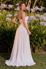 A woman wearing a strapless white A-line wedding gown with lace-up back detailing, standing outdoors in a garden with green foliage and purple flowers.