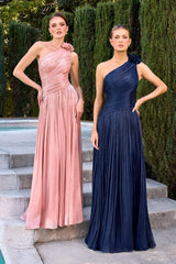 Two women in one-shoulder evening gowns standing on steps with greenery in the background.