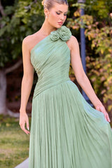 Woman wearing a green one-shoulder dress with a floral detail, standing outdoors.