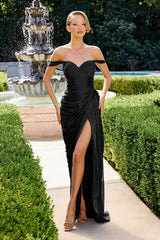 Woman in a black off-shoulder gown standing in front of a fountain with greenery.