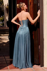 A woman stands with her back to the camera wearing a strapless dusty blue formal gown with a corset-style bodice and lace-up back, posed in front of a dark wooden doorway.