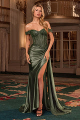 A woman models an off-the-shoulder green satin evening gown with a beaded corset bodice and a high thigh slit, set in an elegant indoor venue with a patterned carpet.