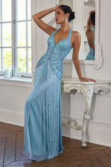 A woman models a light blue evening gown with a beaded bodice and pleated skirt, leaning against an ornate white console table in a bright room with a mirror.
