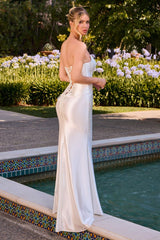 A woman wearing a strapless ivory satin mermaid gown with lace-up back details, standing by a swimming pool in a garden setting.