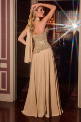 A woman models a floor-length beige evening gown with a heavily embellished beaded bodice and a draped matching shawl, set against a dark interior doorway with dramatic lens flare effects.