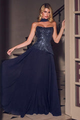 A woman models a strapless navy blue evening gown with a heavily embellished, sequined corset-style bodice and a flowing chiffon skirt, posed in a doorway.