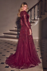 A woman wearing a long-sleeved burgundy tulle evening gown with lace and sequin embellishments, standing in a grand staircase hallway.