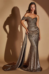 A woman models a strapless off-the-shoulder evening gown with a shimmering metallic bronze finish, featuring a sweetheart neckline, ruched bodice, and a long draped train against a warm beige studio backdrop with a prominent shadow.