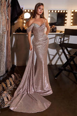 A woman models a sparkling off-the-shoulder evening gown in a dressing room. The floor-length mermaid-style dress is covered in shimmering rose-gold sequins with a fitted silhouette and a long train.