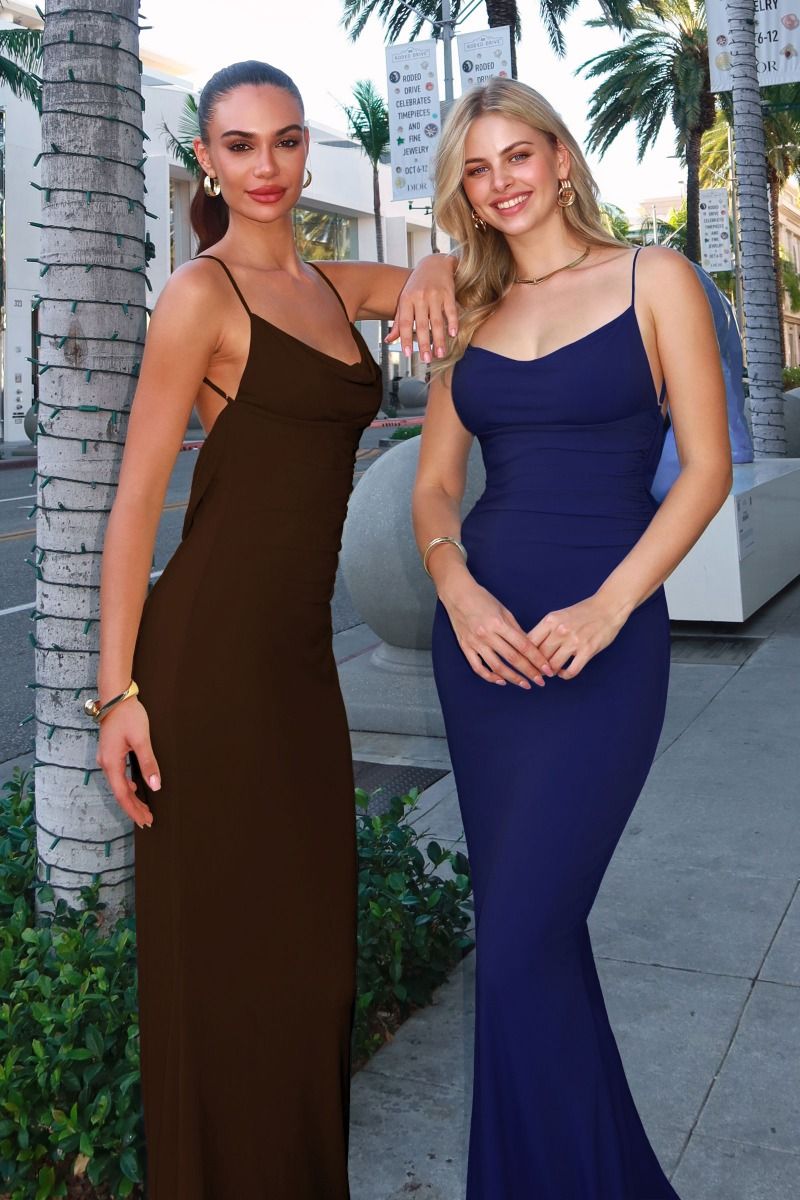 Two women in evening gowns standing next to a palm tree on a city street.