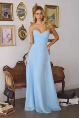 Woman in a light blue dress standing in an elegant room with decorative chairs and mirrors.