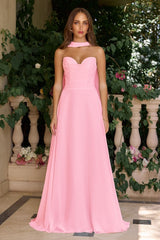 Woman wearing a pink strapless gown standing outdoors with greenery and flowers in the background