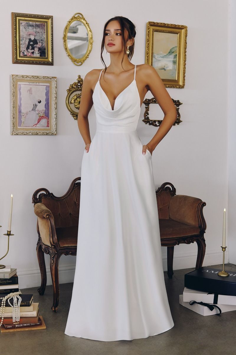 Model wearing a satin gown with draped cowl neckline, fitted waist, and floor-length skirt, featuring thin crisscross straps and open back