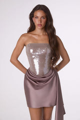 Woman wearing a strapless, sequined dress with a draped front on a white background
