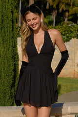 Woman in a black dress and gloves standing outdoors with greenery in the background