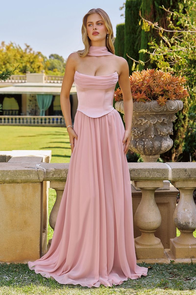 Woman in a pink dress standing outdoors with greenery in the background