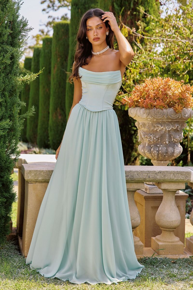 Woman in a sage strapless gown standing outdoors with greenery in the background
