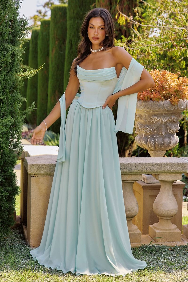 Woman in a sage strapless gown standing outdoors with greenery in the background