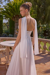 Woman in a white dress with a cape standing outdoors.