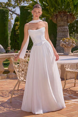 Woman in a white strapless gown standing outdoors with greenery and a table in the background