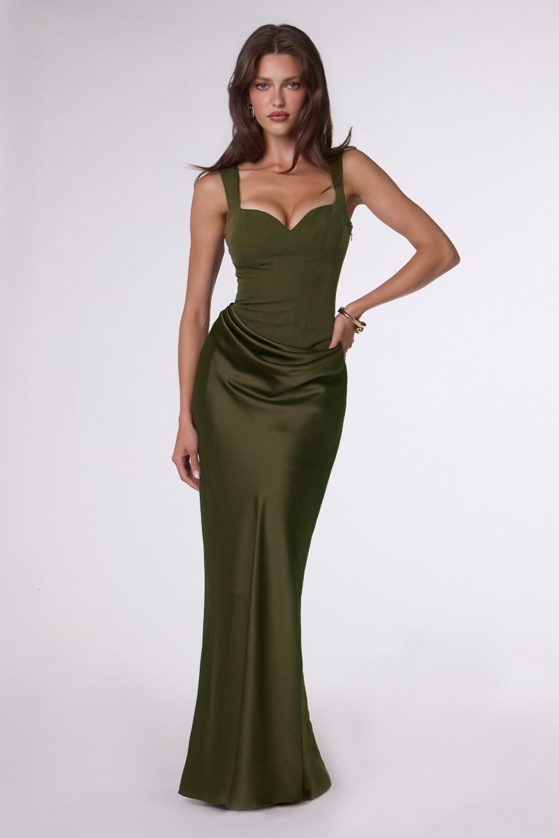 A woman modeling a floor-length olive green satin gown with a sweetheart neckline, thin shoulder straps, and a fitted silhouette against a plain light gray studio background.
