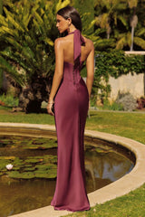 Woman in a burgundy evening gown standing by a pond with greenery in the background