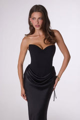 Woman wearing a black strapless gown with a draped effect on a white background
