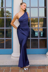 Woman in a blue one-shoulder dress standing in front of a building with large windows.