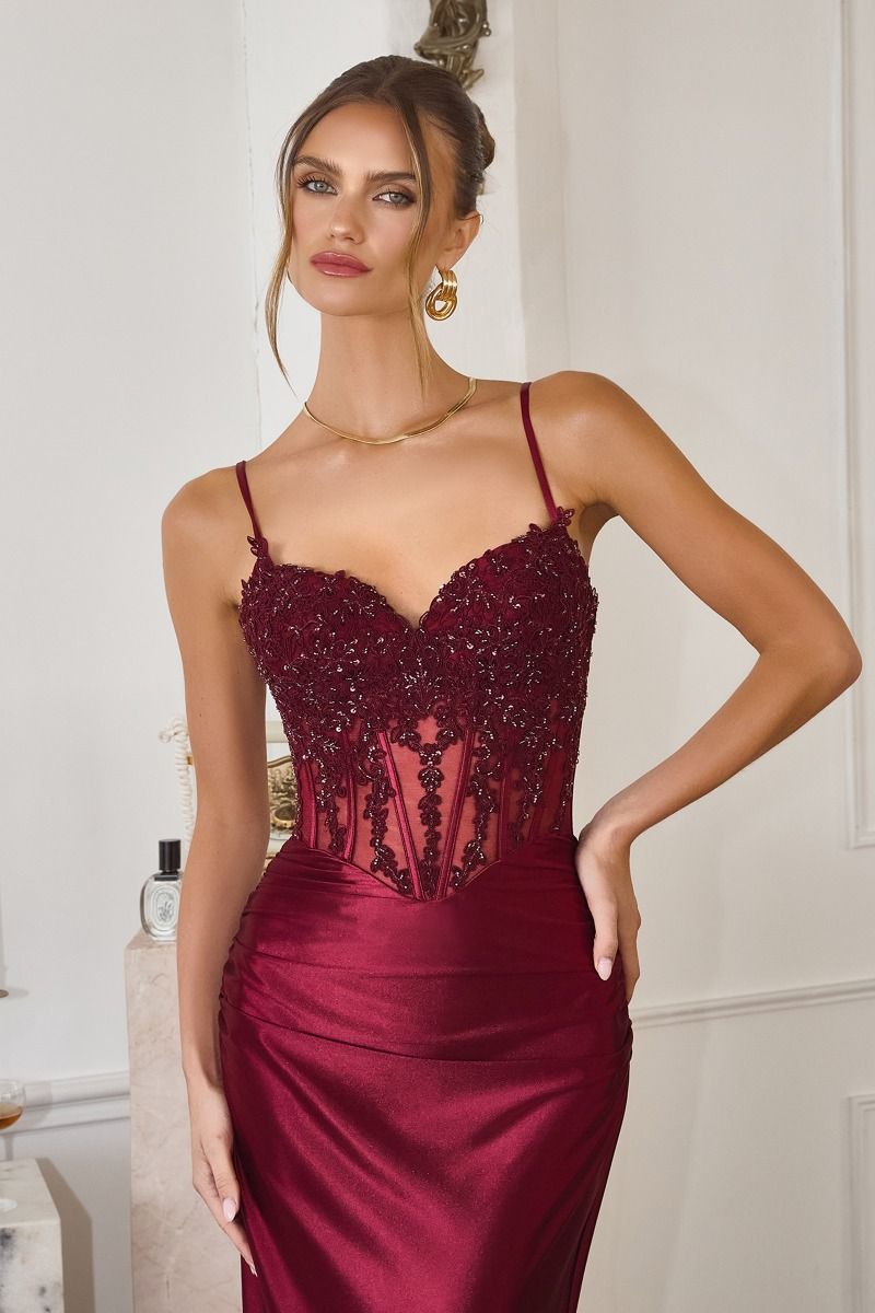 Woman wearing a burgundy evening gown with lace details in an elegant indoor setting.