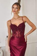 Woman wearing a burgundy evening gown with lace details in an elegant indoor setting.